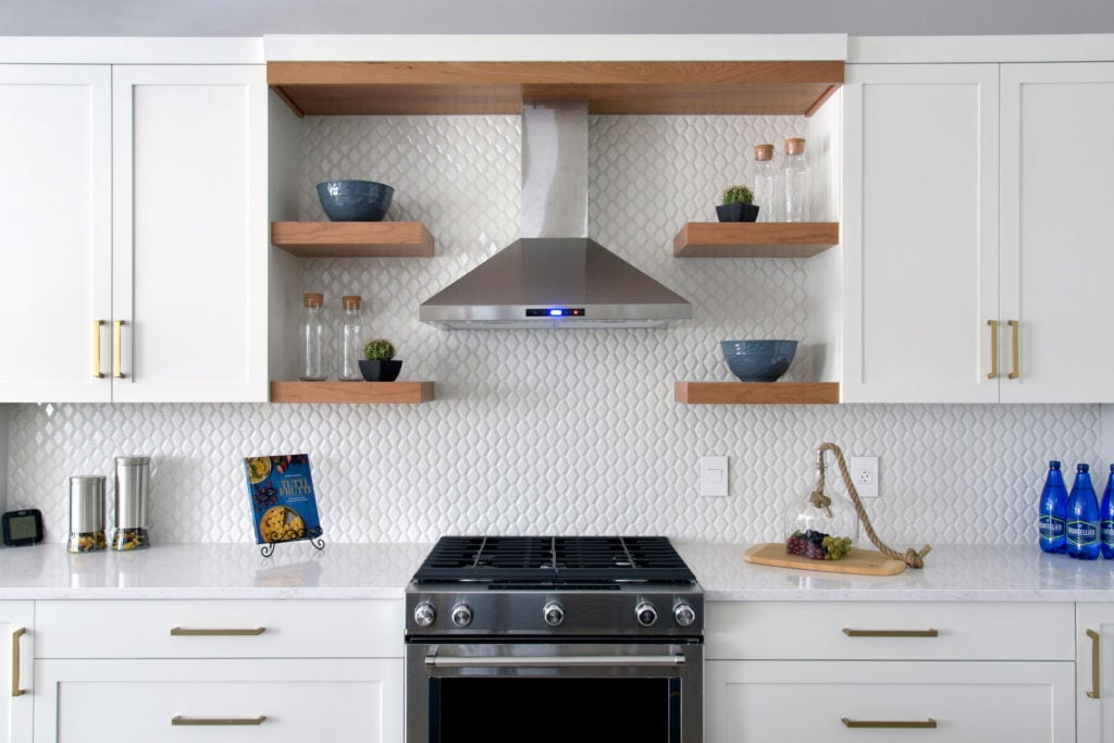 A custom kitchen with a tiled backsplash, floating shelves, and range hood.